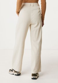 Cream corduroy wide-leg pants with a ribbed texture and high waist, paired with olive and gold sneakers.
