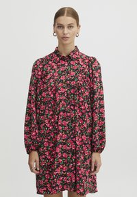 Abito floreale nero con motivi rosa e verdi, maniche lunghe, spalle arricciate e pattina con bottoni. Tessuto morbido e leggero.