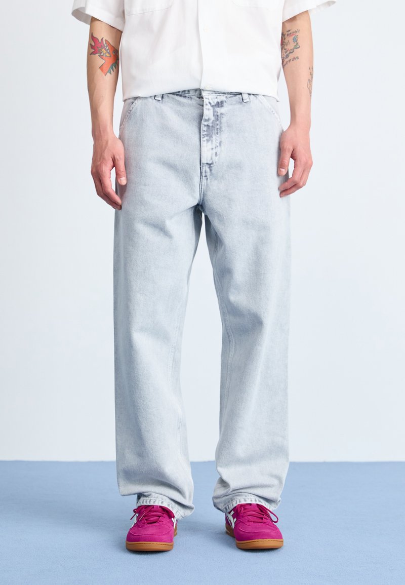 Lyseblå denimjeans med løs passform, med knapp og glidelås lukking, samt frontlommer, kombinert med klare rosa joggesko.