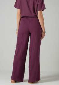 Pantalon large violet en tissu froissé, dotés d'une coupe décontractée et d'une taille élastique ; associés à un haut à manches courtes assorti.