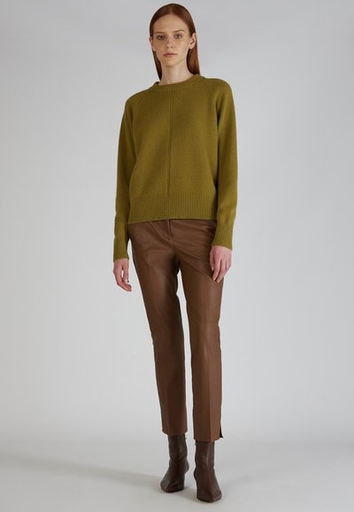 Olijfgroen wollen trui met ribbelmanchetten, gecombineerd met strakke bruine leren broek met enkelopeningen en elegante bruine haklaarzen.