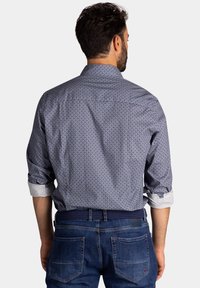 Marineblauwe blouse met patroon en opgerolde mouwen, met knoopsluiting, gemaakt van lichtgewicht stof; gecombineerd met donkerblauwe jeans en een gevlochten riem.
