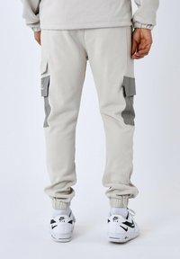Licht grijze cargobroek met elastische manchetten en zijzakken; heeft een gestructureerde stof en contrasterende grijze details. Gekoeld met witte sneakers.