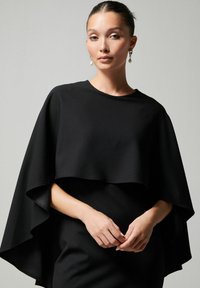 Mustasat päikesekaitsekleit, millel on mugav lõige. Sile tekstuuriga kangas langeb elegantse ilu poole, omades ümarat kaelust ja kihilist disaini.