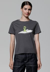 Grijze katoenen t-shirt met een afbeelding van een groene alien die op een wit papieren vliegtuigje zit, met een sterry achtergrond. Korte mouwen.