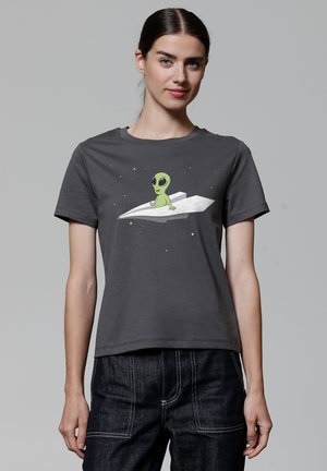 T-shirt en coton gris avec un graphisme d'un alien vert assis sur un avion en papier blanc, avec un fond étoilé. Manches courtes.