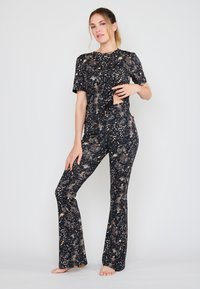 Conjunto atlético de tie-dye negro y dorado que incluye una camiseta de manga corta y leggings acampanados, fabricado con un tejido elástico y texturizado.