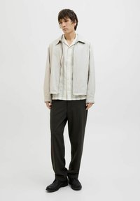 Lichtgrijze jas met een gladde textuur, colbert met verticale strepen, donkere broek en zwarte schoenen. Eenvoudig, modern ontwerp.