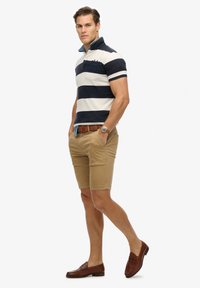 Marineblauwe en witte gestreepte polo met kraag, gecombineerd met khaki shorts en bruine instappers. Bevat een riem en een polshorloge.