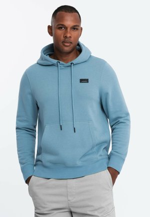 Felpa con cappuccio di colore azzurro chiaro in morbido tessuto, con tasca anteriore, cordini di regolazione e un'etichetta nera sulla parte anteriore.