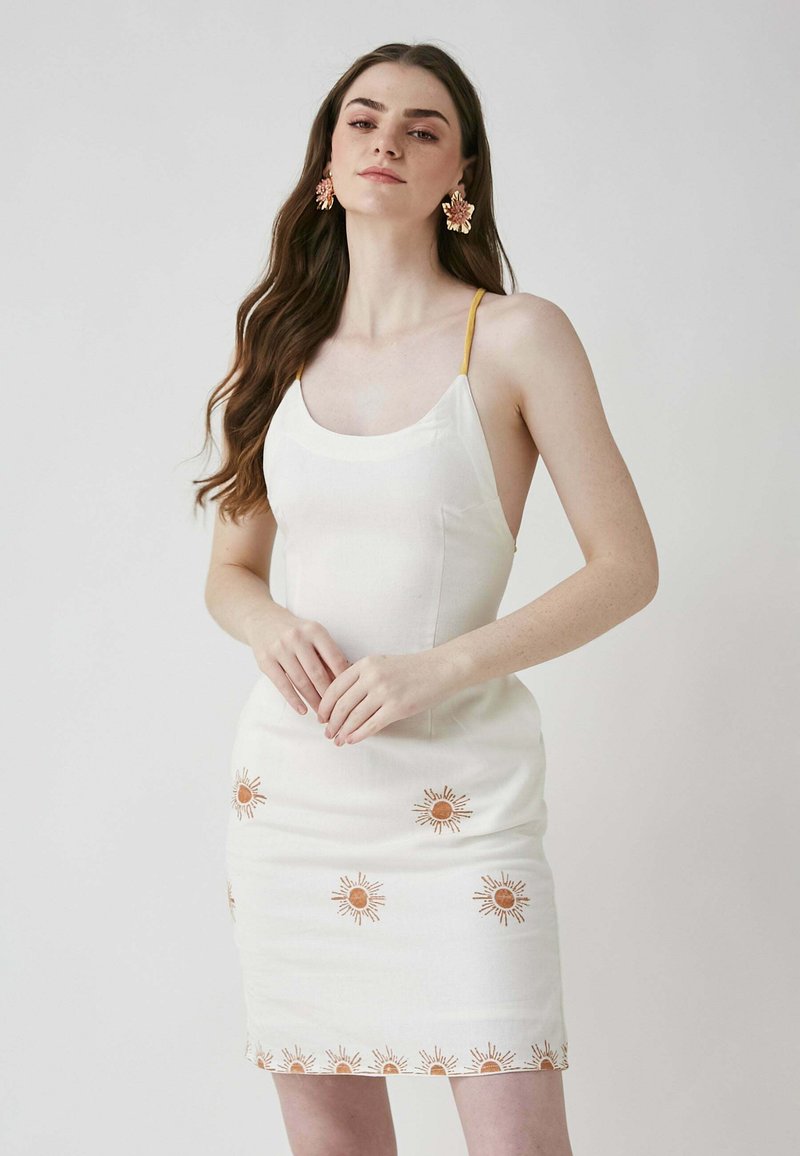 Weißes Kleid mit Spaghettiträgern, mit orangefarbener Sonnen-Stickerei am Saum und verteilt über das Kleid, glatte Textur, figurbetonte Silhouette.