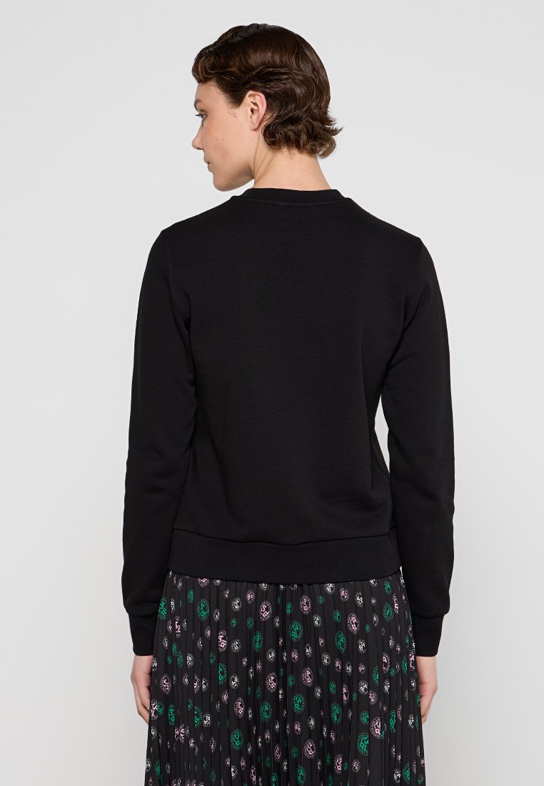 Sudadera negra con cuello y puños de canalé, que cuenta con una cintura ajustada. Combinada con una falda plisada con estampado.