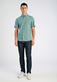Kurzärmliges, hellblaues Hemd aus strukturiertem Stoff, kombiniert mit dunkelblauen Jeans und weißen Sneakers. Einfacher Kragen, normale Passform.