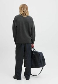 Mørkegrå strikket sweater med en afslappet pasform, parret med mørke bukser. Modellen har en sort duffeltaske med en tekstureret overflade og håndtag.