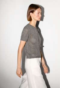 Szary sweter o krótkim rękawie z fakturowanym wykończeniem, w zestawie z białymi, luźnymi spodniami. Do stroju dodano prosty naszyjnik.