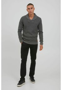Suéter gris de punto con un amplio cuello de chal y un patrón texturizado, combinado con pantalones negros ajustados y zapatillas negras.