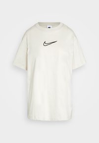 Krämfärgad bomull T-shirt med rund halsringning, korta ärmar och en svart Nike swoosh-logotyp broderad på bröstet.