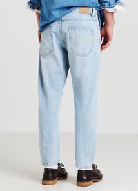 Jeans in denim azzurro chiaro con vestibilità rilassata, dotati di due tasche posteriori, texture leggermente sbiadita e un'etichetta in pelle marrone sulla vita.