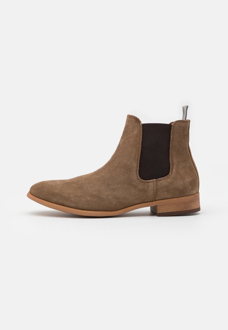 Botte Chelsea en daim marron avec panneau latéral élastique noir, talon bas en bois et languette de tirage sur fond blanc.