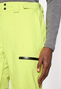 Λάιμ πράσινα παντελόνια σκι με κομψό σχεδιασμό, αντίθετη μαύρη τσέπη με φερμουάρ, ανθεκτικούς βραχίονες ζώνης και λείο, υφαντό ύφασμα.