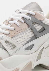 Baskets avec un mélange de mesh blanc, de suède taupe et d'accents gris. Design à lacets avec découpes sur le côté et semelle texturée.