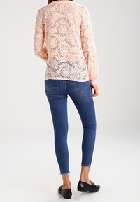 Verkkopusero vaalean persikan värissä kukkakuviolla, pitkät hihat; yhdistetty sinisiin kapeisiin farkkuihin ja mustiin tasapohjaisiin kenkiin.