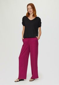 Zwarte gebreide V-hals top met korte, opgerolde mouwen, gecombineerd met high-waisted, wijde broekspijpen in levendig fuchsia, voorzien van zijzakken.