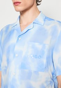 Ljusblå kortärmad skjorta med tie-dye mönster, som har en bröstficka med "HUGO"-logotyp. Slät tyg med knäppning.