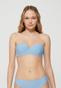 Top de bikini bandeau en azul claro con una textura suave, copas moldeadas y sin tirantes. Diseño minimalista con un sutil brillo. Emparejado con braguitas a juego.