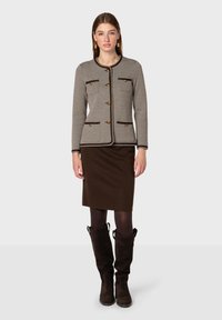 Grå hundtandjacka med guldfärgade knappar, brun kant och fickor, i kombination med en åtsittande brun kjol och bruna knähöga stövlar.