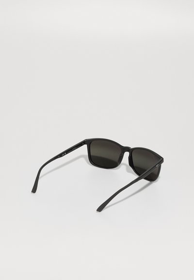 Svarte solbriller med firkantet design, mørke linser og slanke matte rammer. Inkluderer understated merking på innsiden av brillestengene.