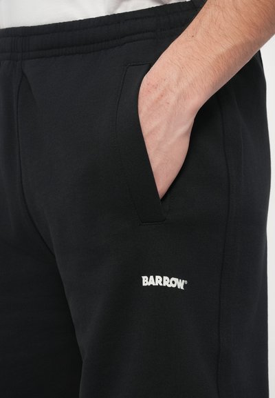 Pantaloni sport negri cu talie elastică, buzunare laterale și logo alb "BARROW". Material moale, cu textură netedă.