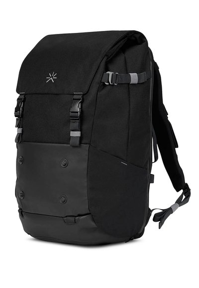 La mochila negra presenta un cuerpo de tela suave con un fondo negro mate, correas ajustables y cierres a presión. Diseño minimalista con detalle del logotipo.