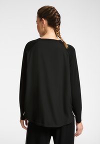 Top negro de manga larga con dobladillo redondeado, cuello acanalado y mangas raglán, con una textura suave y un corte relajado.