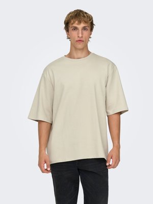 Beige oversized cotton t-shirt with short sleeves and a round neckline, paired with dark jeans. Smooth texture and relaxed fit.