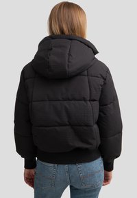 Juodas pūkinis švarkas su tekstūruota tinklelio raštu, kurį papildo gobtuvas, elastiniai rankogaliai ir prigludęs apačios kraštas. Tinka žiemiškoms oro sąlygoms.