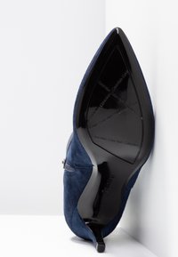 Navyblauwe suede hoge hak met een spitse neus en een zwarte glanzende zool, met een textuurafwerking en Calvin Klein branding op de zool.
