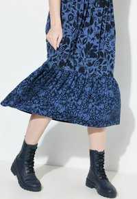 Niebieska sukienka w kwiatowy wzór z falbanami przy hemie, zestawiona z czarnymi kowbojkami na sznurowadła. Gładka tekstura materiału, długość do kolan.