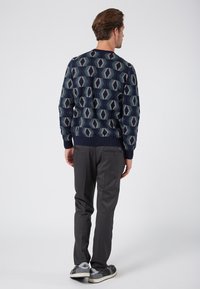 Navy sweater with geometric pattern, ribbed cuffs and hem. Grey pants with two back pockets, worn with grey and black sneakers.