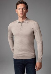 Beige Langarm-Polohemd aus weichem Strickmaterial mit klassischem Kragen, einer Drei-Knopf-Leiste und gerippten Bündchen, kombiniert mit dunkelblauen Denim-Jeans.