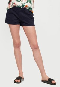 Marinblå bomullsshorts med en rak front, två sidofickor och en avslappnad passform. Kombineras med svarta flip-flops.
