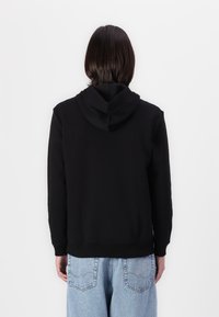 Sweat à capuche noir avec cordon de serrage, bord-côte en bas et aux poignets, associé à un jeans bleu clair ample. Design simple avec une texture lisse.
