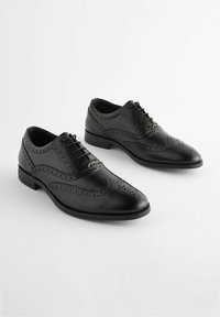 Zapatos de vestir de cuero negro con detalles de brogue, punta redonda, diseño con cordones y acabado liso. Suela de goma con tacón bajo.