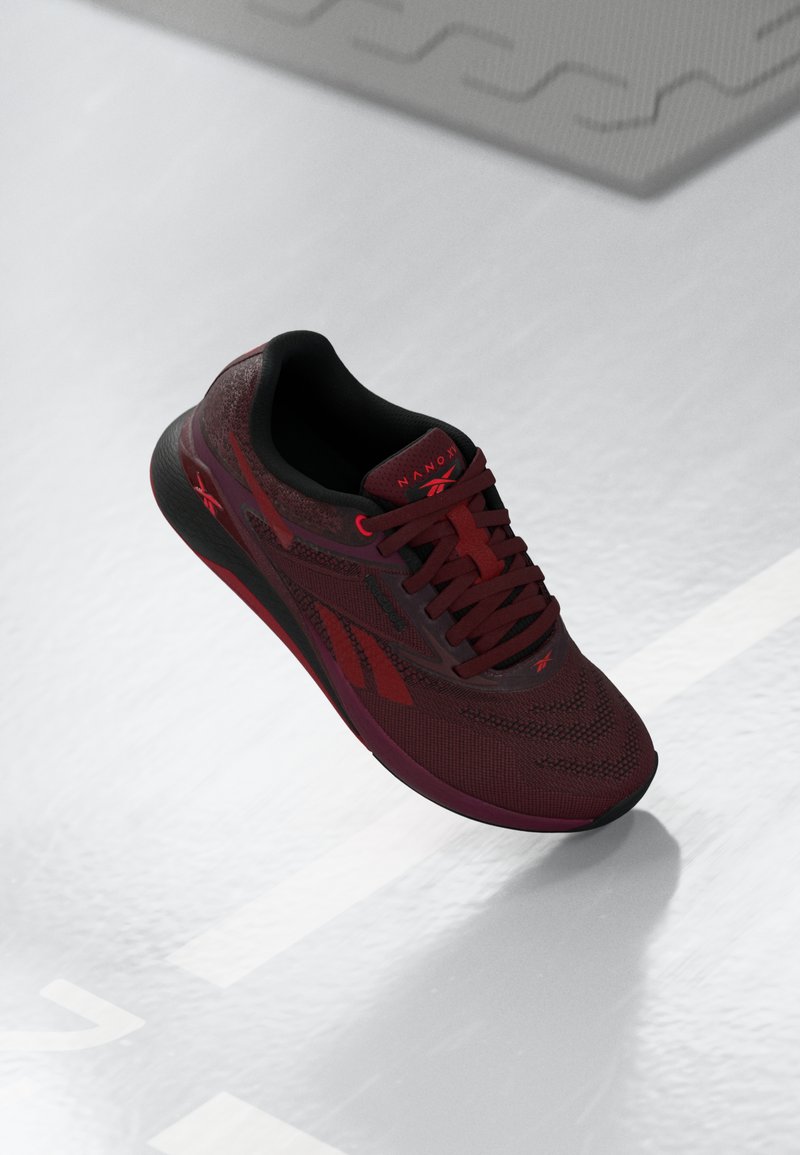 Scarpa sportiva bordeaux con tomaia in maglia testurizzata, dettagli neri e suola flessibile. Presenta un logo ben visibile e lacci in tono.