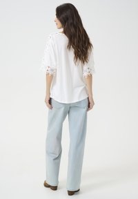 Hvid top med blonderør på de brede ærmer, parret med lyseblå straight-leg jeans og brune hælede støvler. Enkel, afslappet outfit.