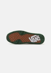 Vans sneakersål med grøn og brun gummi, der har et diamantmønster og et hvidt logo. Textureret overflade for bedre greb.
