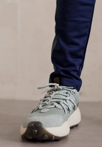 Sneaker azzurro chiaro con tomaia testurizzata, lacci flessibili e suola bianca e ammortizzata. Indossato con pantaloni navy a sigaretta.