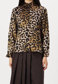 Bluse im Leopardenmuster mit goldenen, schwarzen und rosa Tönen, mit Kragen und langen Ärmeln, aus einem glatten Stoff gefertigt.