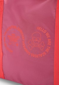 Bolsa de tela rosa con un gráfico brillante en color naranja que presenta una calavera y dos huesos cruzados, y un texto que dice "Hola, somos la empresa Scalpers."