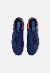 Zapatos de fútbol color azul marino con una parte superior texturizada, que presentan un acento naranja vibrante y un logotipo azul. Diseño con cordones y forma redondeada.